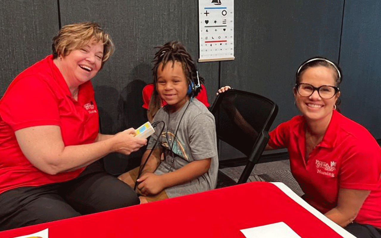 two women in fsc uniforms with a child wearing headphones attached to a device