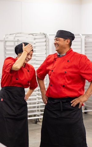 Young woman and older man laughing together in chef attire
