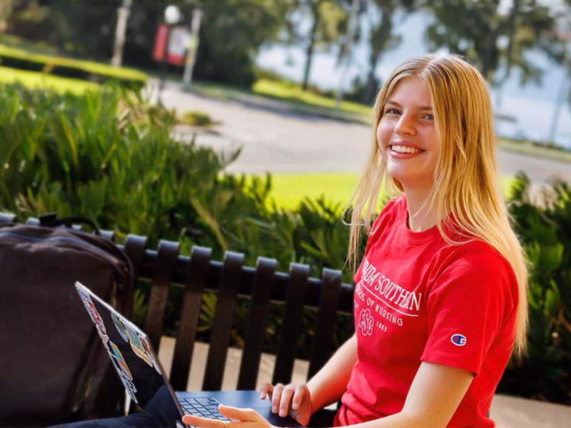 student working on laptop outside sitting on bench